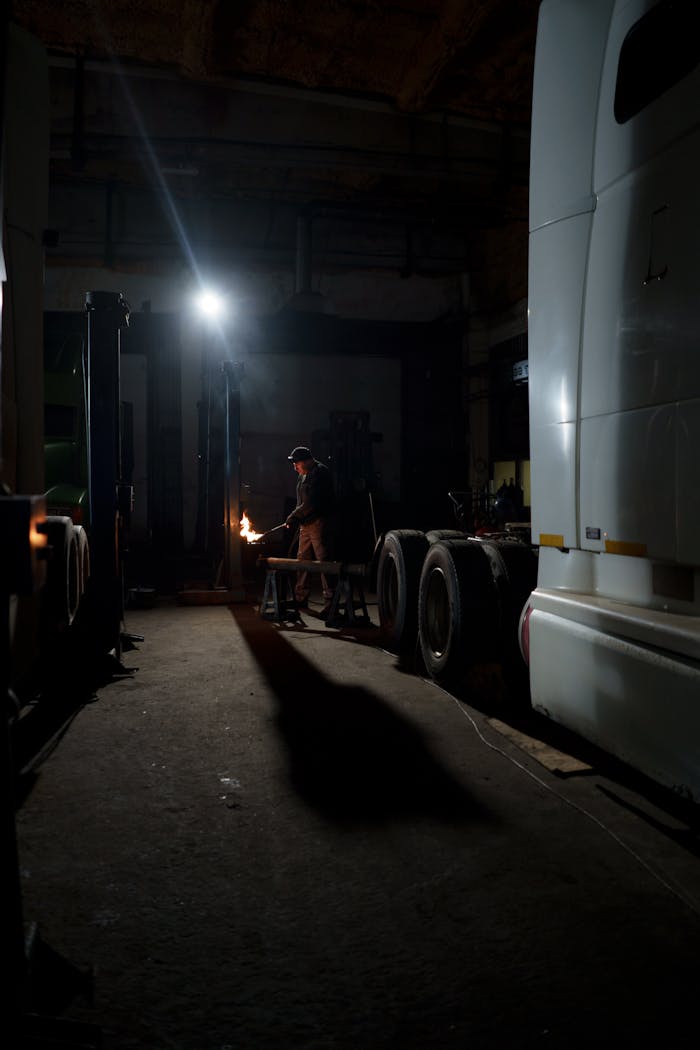 cta-02 A welder works on a truck in a dimly lit garage, creating sparks.