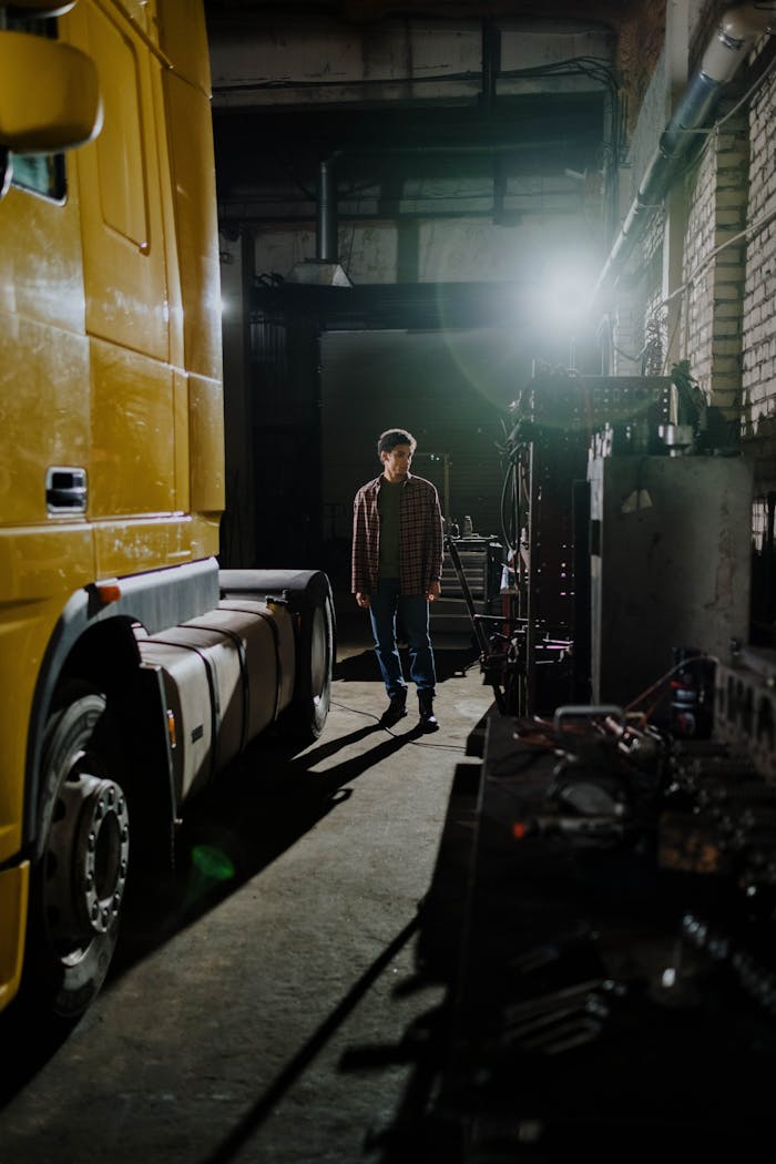 gallery-03 Auto mechanic standing near a truck inside a dimly lit garage, emphasizing industrial workspace.