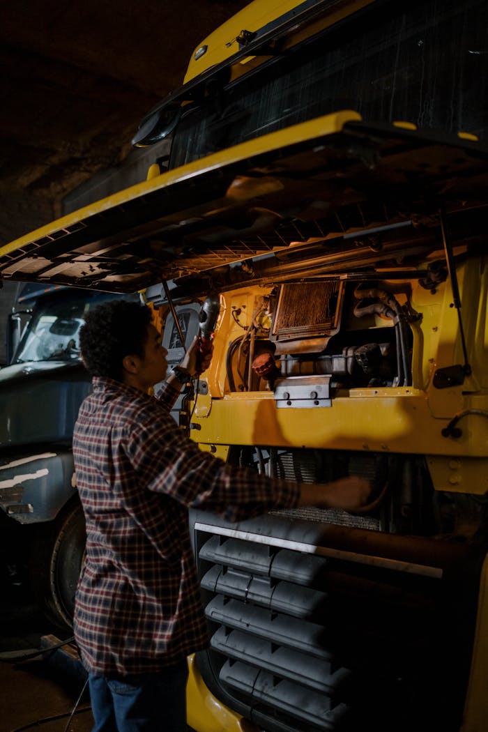 portfolio-01 A mechanic works on a truck engine in a dimly lit garage, focusing on repairs.