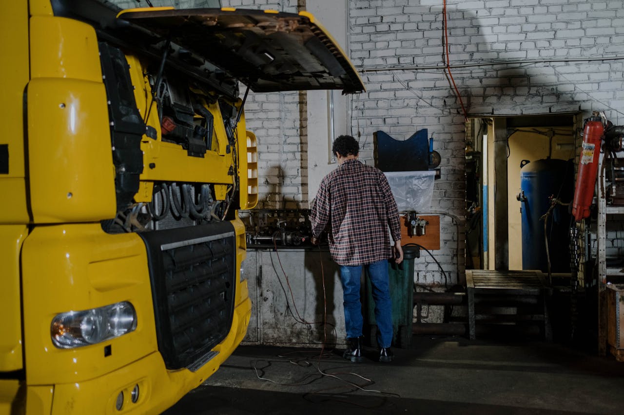 gallery-05 A mechanic working on a yellow truck engine in an indoor garage setting.